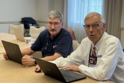 two men with laptops looking up at camera