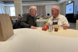 two men sitting in a room eating lunch