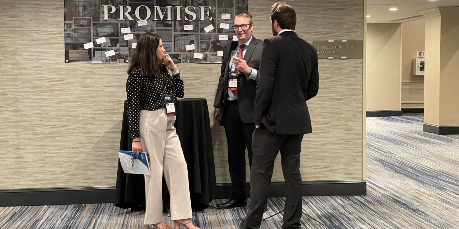 a woman and two men in a hallway in front of a board with the words Promise and multiple cards