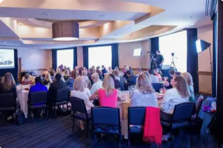 A picture of people sitting at tables looking at a presentation.